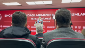kırmızı fonlu sahnede konuşma yapıyorum. Arka planda “Engelli Vatandaşlarımızın Kamu Kurumlarına Yerleştirilmesi Töreni” yazısı yer alıyor. Betimleme: ChatGPT yapay zeka